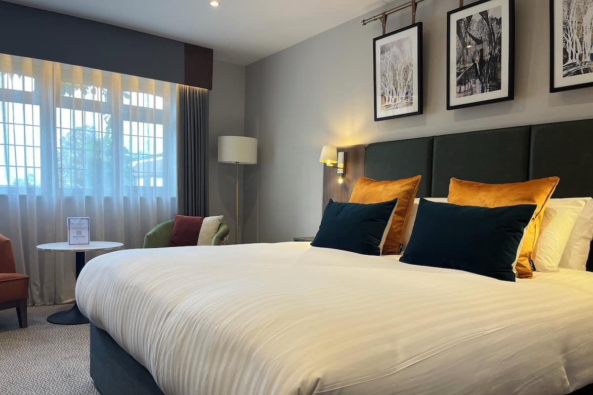 Een hotelkamer met een groot bed, een bureau met stoel, een lamp en lijstjes met foto's aan de muur.