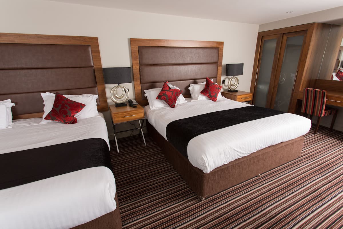 Een hotelkamer met twee bedden, houten hoofdeinden, een gestreept tapijt en een kledingkast.