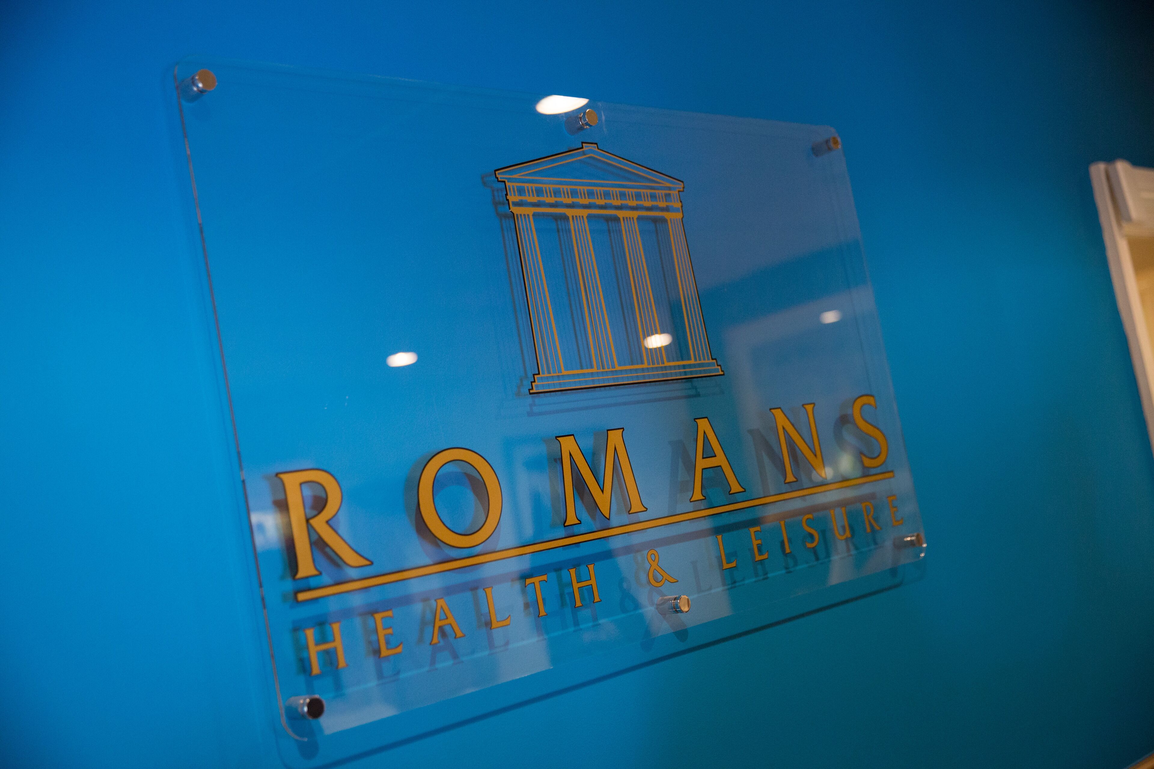A clear glass sign with the name "ROMANS HEALTH & LEISURE" and a classical building icon.