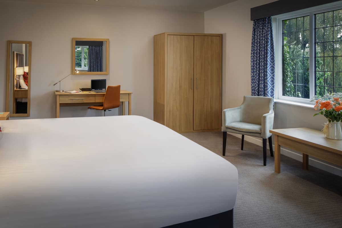 Een hotelkamer met een groot bed, een bureau, een stoel, een kledingkast en een raam met gordijnen.