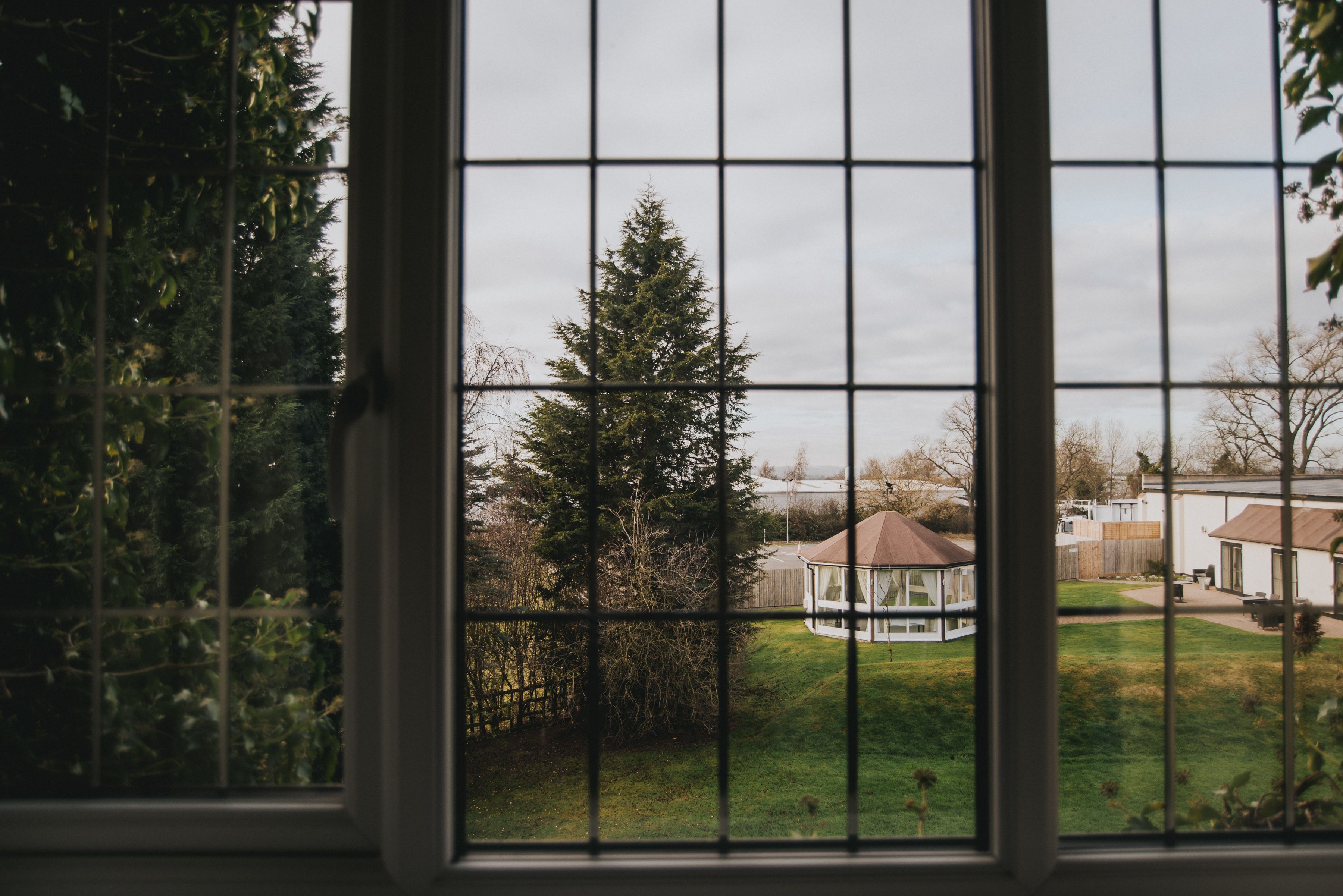A view through a window with a grid pattern, revealing a gazebo in a yard with a lawn and trees.