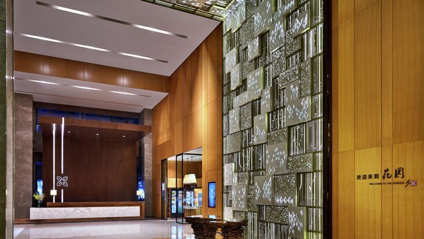 Un vestíbulo moderno con una recepción, un panel de vidrio y una pared de madera con un letrero de bienvenida.