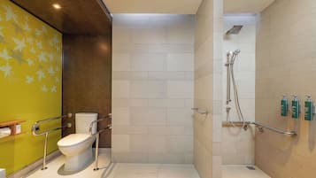 A bathroom with a toilet, a shower with grab bars, and a green wall with leaf patterns.