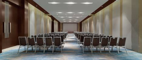 A hotel corridor with rows of chairs, a carpeted floor, and recessed lighting.