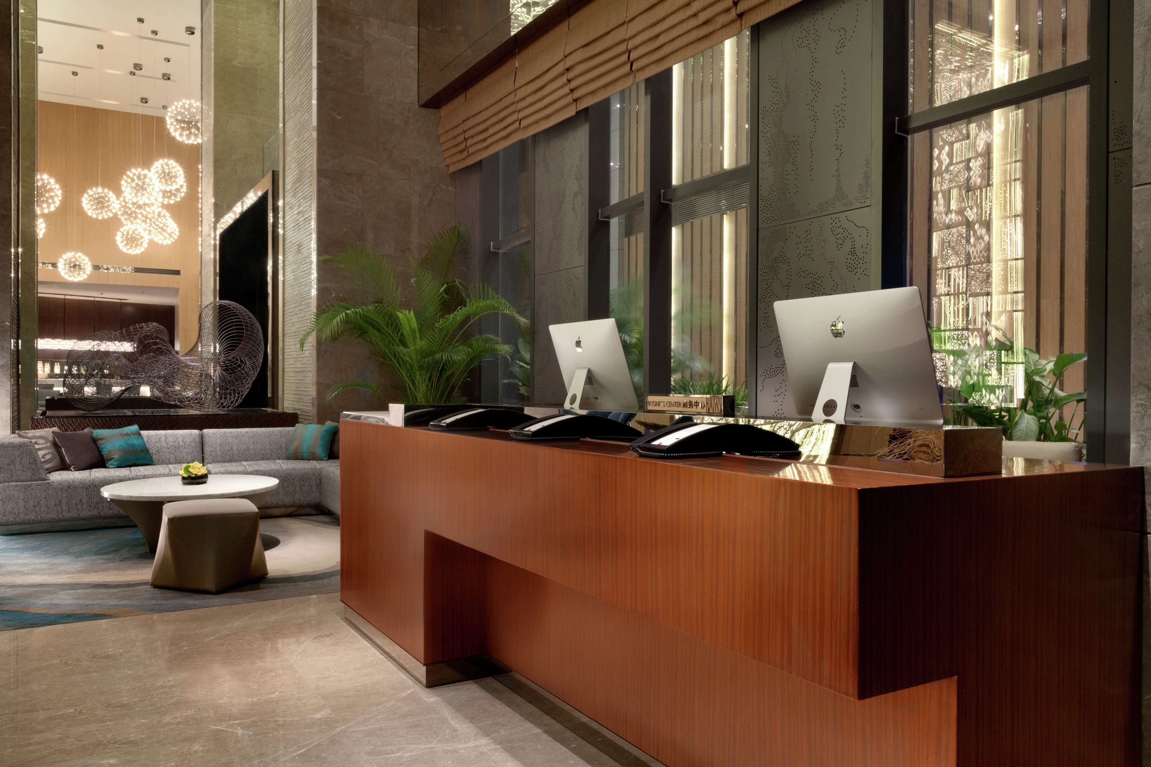 A modern reception desk with Apple iMacs, a sofa, and a coffee table in a lobby with large windows and decorative lighting.