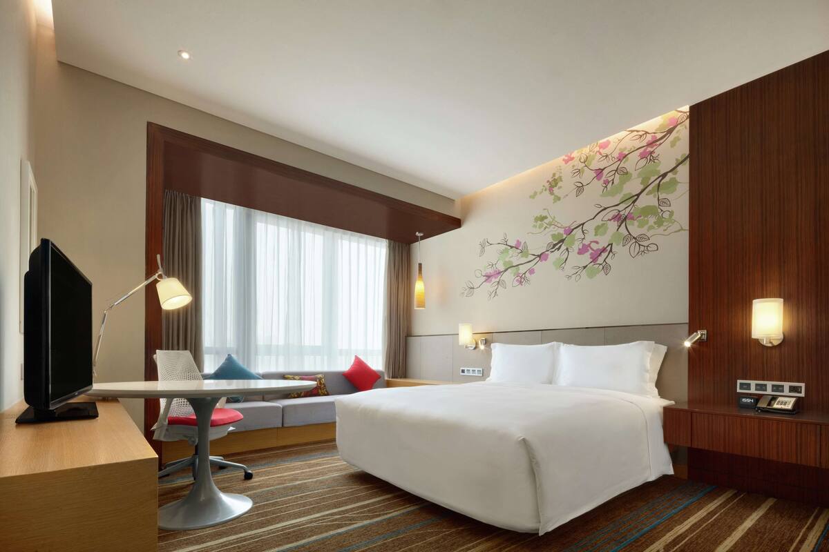 Una habitación de hotel con una cama grande, un escritorio con silla, un televisor y una ventana con cortinas.