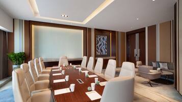 A conference room with a long table, white chairs, and a projector screen.