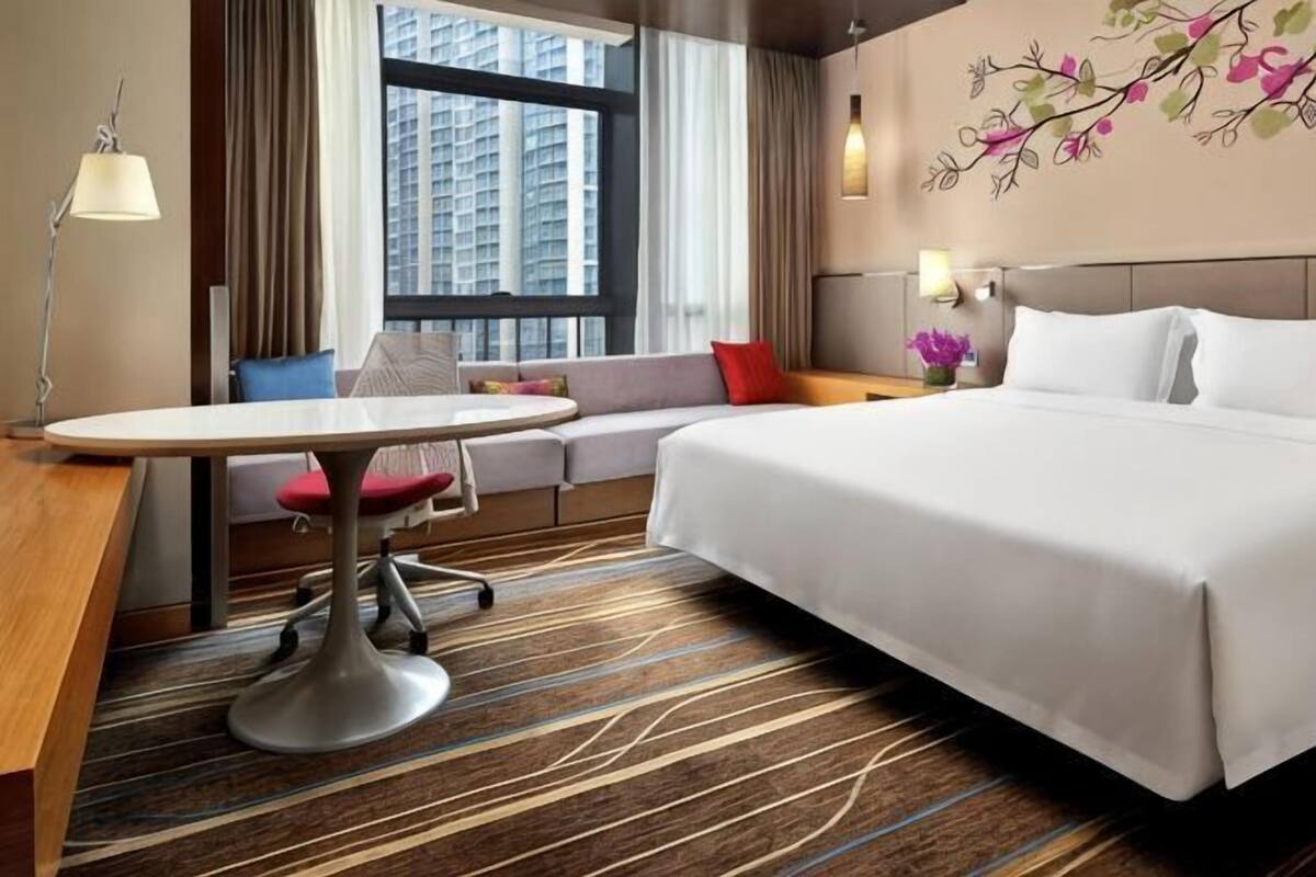 Habitación de hotel con cama, escritorio, silla, sofá y ventana con vista a edificios.