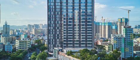 A modern high-rise hotel with a prominent Hilton Garden Inn sign, surrounded by a cityscape with various buildings and a busy street below.