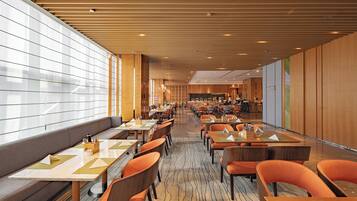 A modern hotel lobby with a long reception desk, multiple seating areas with tables and chairs, and a patterned floor.