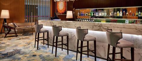 A bar area with a marble counter, multiple bar stools, and a variety of liquor bottles.