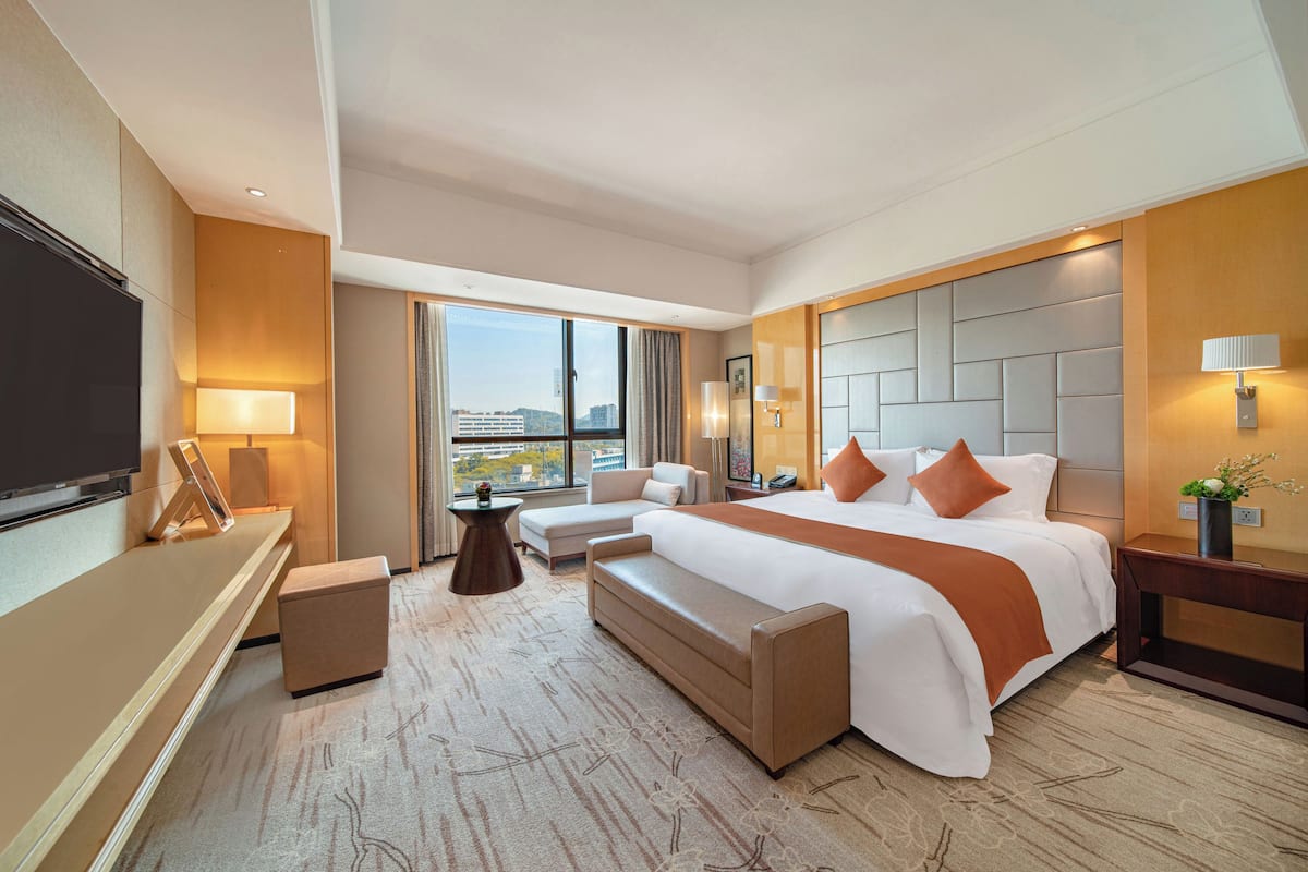 A modern hotel room with a large bed, a sofa, a TV, and a desk.