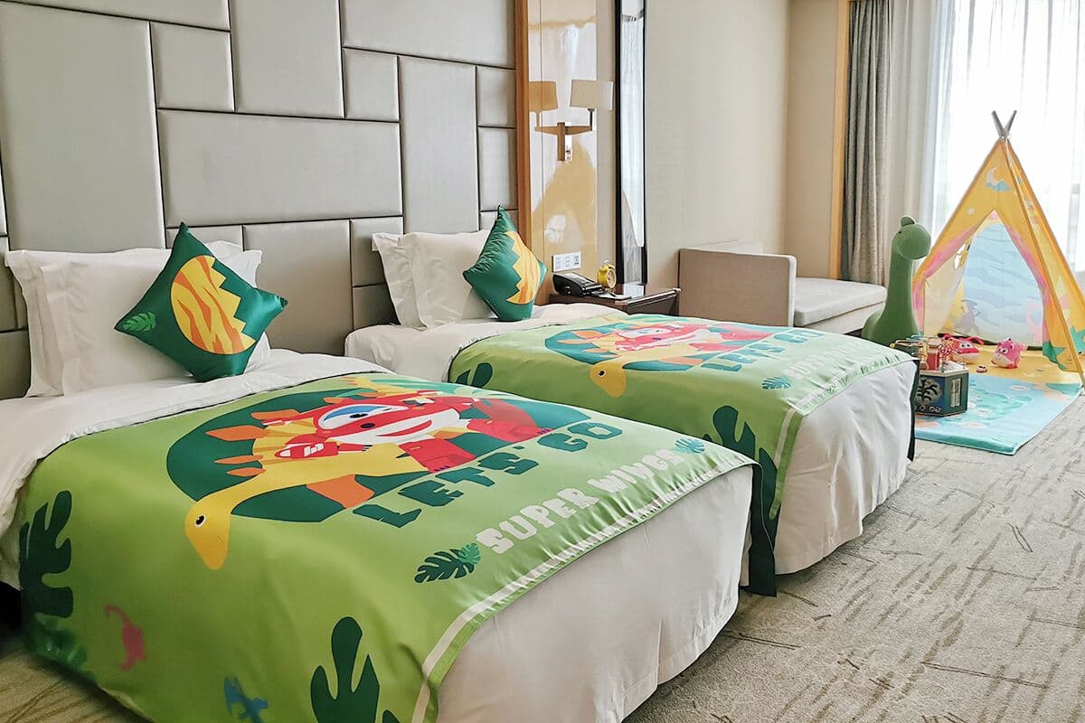 A hotel room with two beds, a green and white color scheme, a tent, and a small play area.
