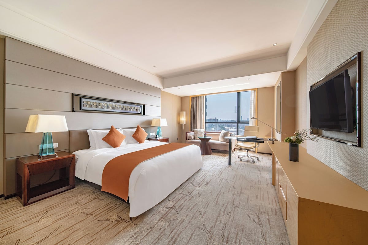 A hotel room with a large bed, a desk, a TV, and a city view.