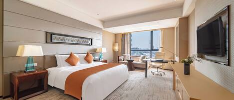 A hotel room with a large bed, a desk, a TV, and a city view.