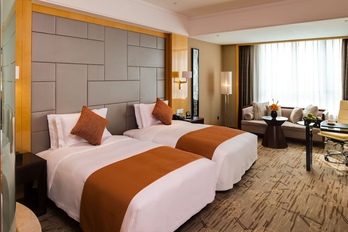 A hotel room with two beds, a sofa, a small table, and a lamp.