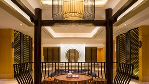A spacious dining area with round tables and chairs, a central chandelier, and decorative screens.