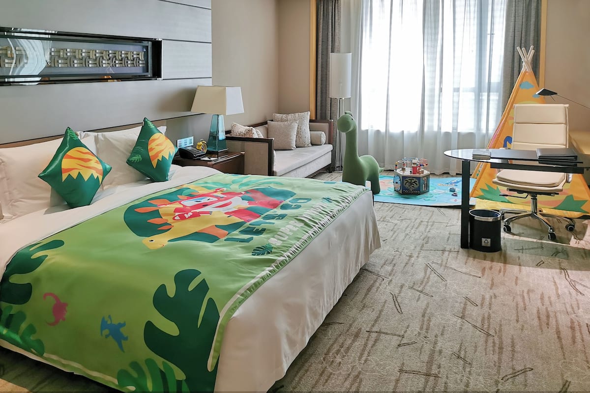 A hotel room with a bed, a sofa, a desk, a lamp, a window with curtains, and a tent.