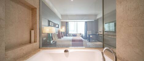 A modern bathroom with a large bathtub, a glass-enclosed shower, and a view of the bedroom through the mirror.