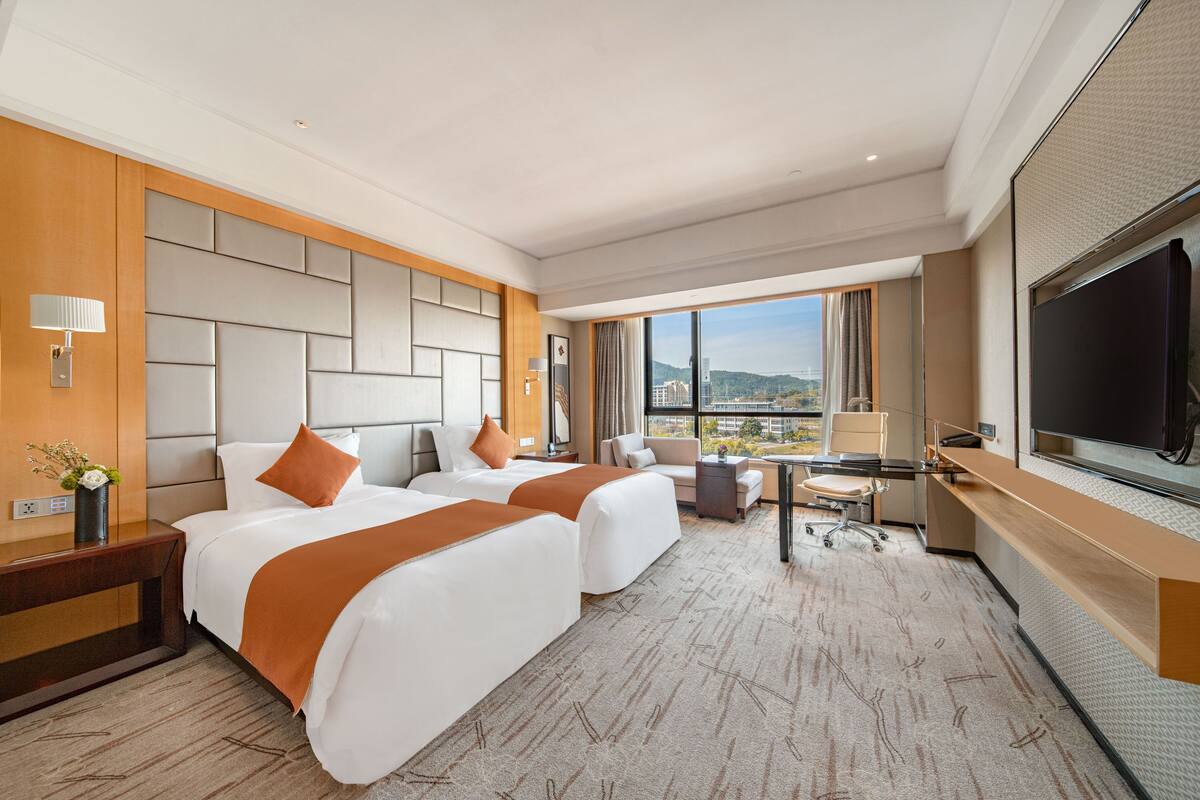 A hotel room with two beds, a desk, a chair, and a large TV.