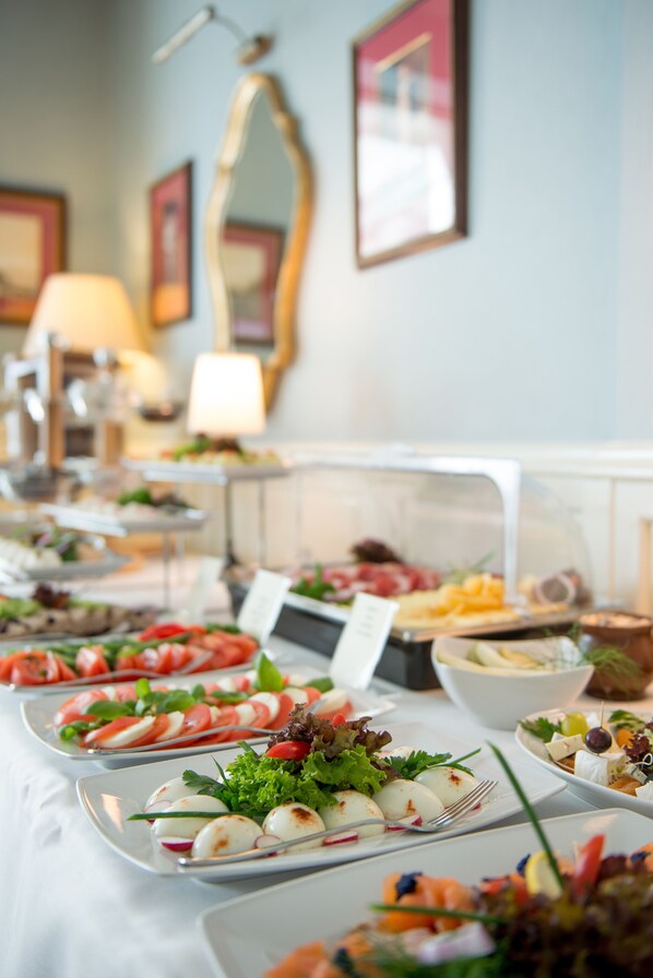 A buffet table with various dishes, including salads and appetizers, in a well-lit room with framed pictures on the wall. - Hotel Kościuszko (Kraków)