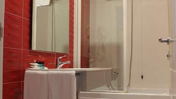 Ein Badezimmer mit roter Wandfliese, einem weißen Waschbecken, einem Spiegel, einer Duschkabine aus Glas und einer weißen Badewanne.