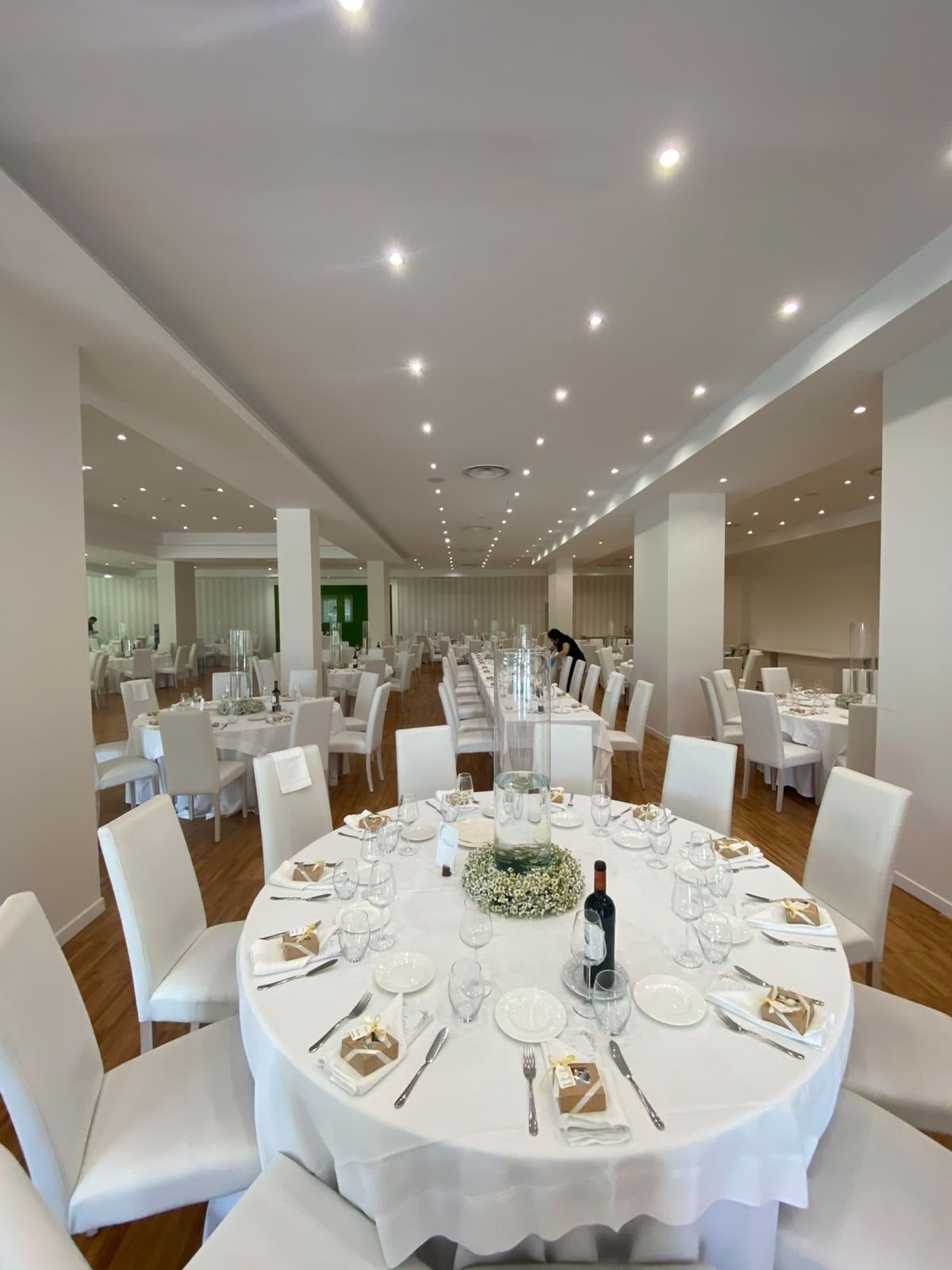 A banquet hall with round tables set for a formal event, featuring white tablecloths, glassware, and floral centerpieces.