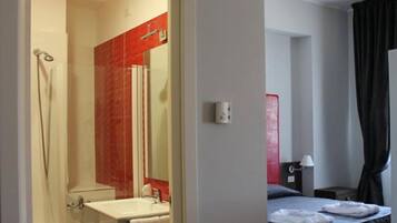 Habitación de hotel con ducha, lavamanos y cama con mesita de noche.