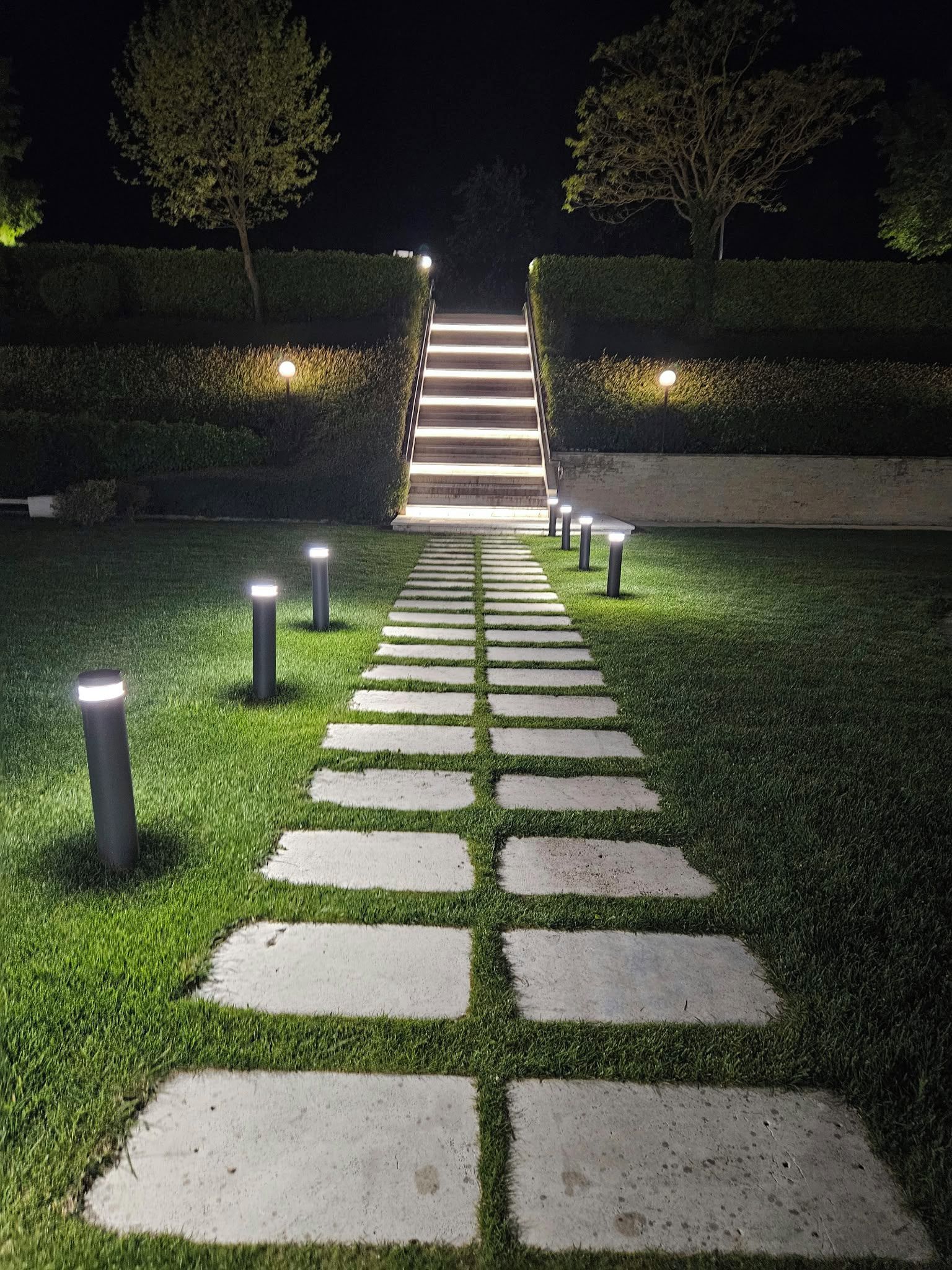 A nighttime pathway with illuminated bollards and a staircase leading up.