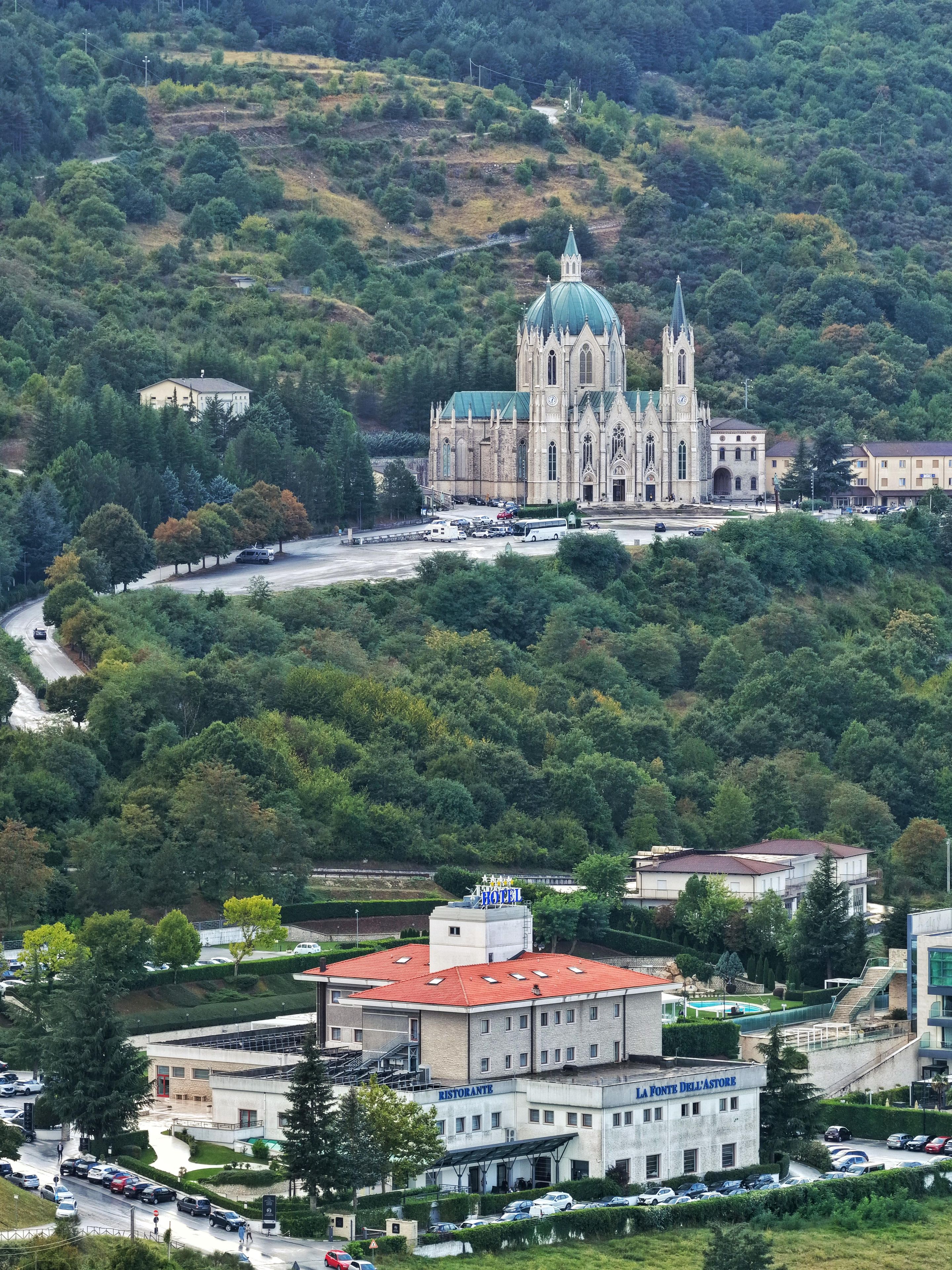 A large building with a prominent dome and spires, surrounded by lush greenery and a winding road.
