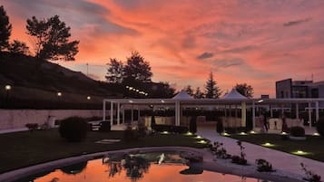 Eine ruhige Außenanlage mit einem Spiegelteich, einem überdachten Pavillon und einem Sonnenuntergangshimmel.