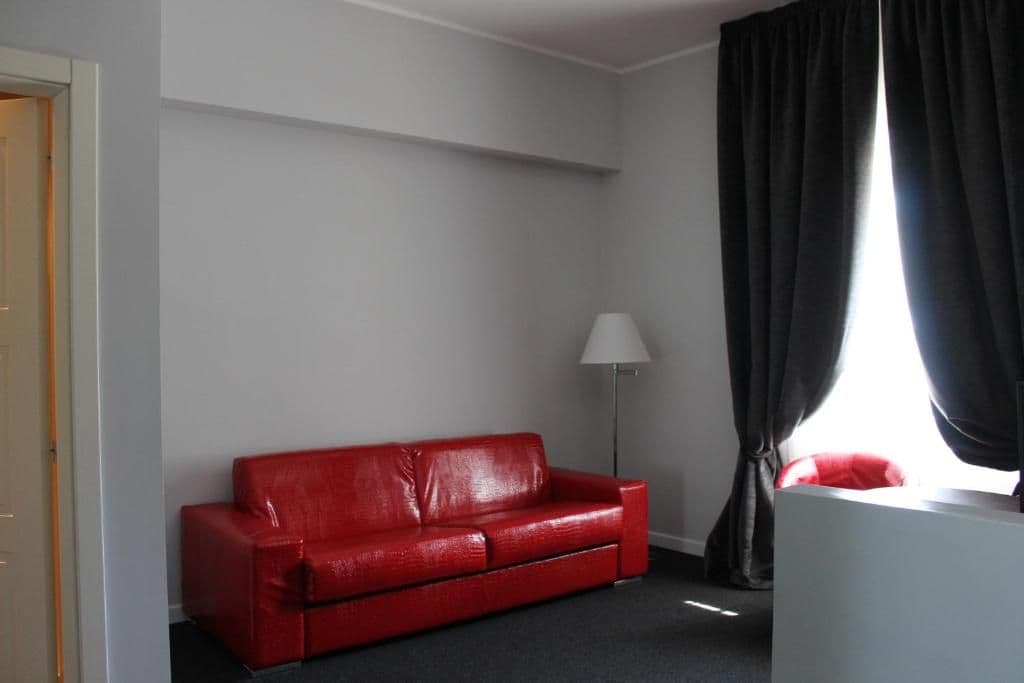 Ein Zimmer mit einer roten Couch, einer Stehlampe und einem Fenster mit Vorhängen.