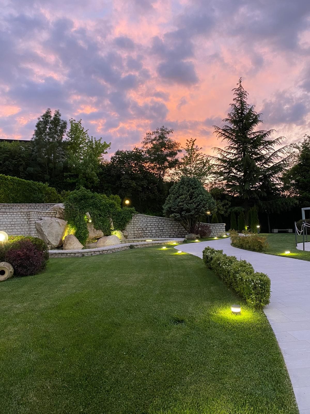 A landscaped garden with a stone wall, a pathway, and a variety of trees.