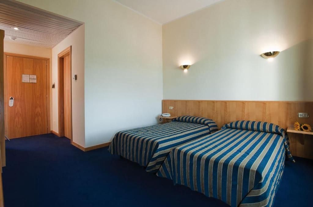 Habitación de hotel con dos camas, un cabecero de madera, una mesita de noche y una lámpara fijada a la pared.