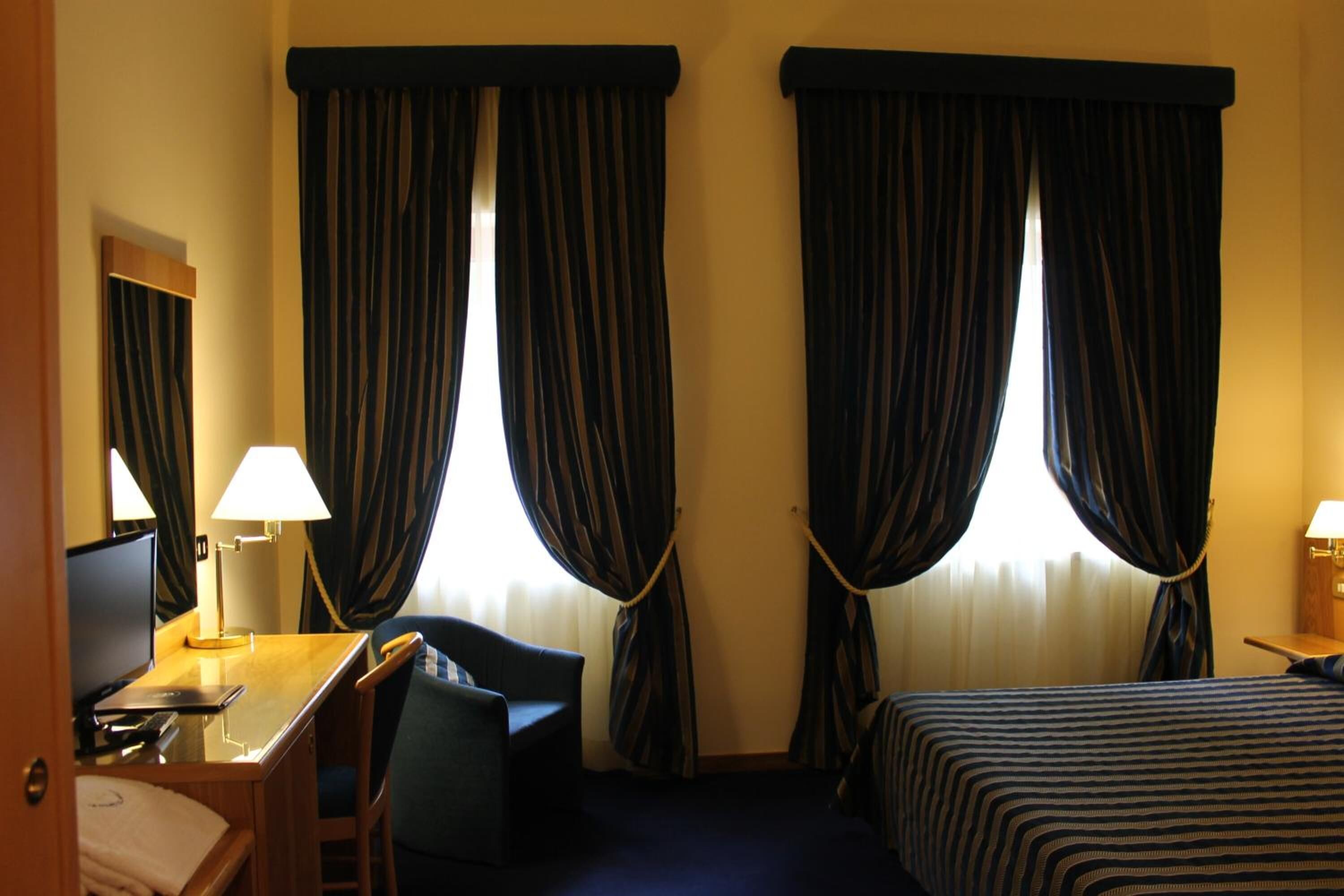 Ein Hotelzimmer mit Bett, Schreibtisch mit Stuhl, Fernseher und Vorhängen.