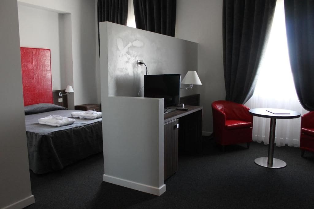 Ein Hotelzimmer mit einem Bett, einem Schreibtisch mit Computer, einem Sessel, einem kleinen Tisch und einem Fernseher.