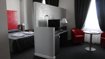 Ein Hotelzimmer mit einem Bett, einem Schreibtisch mit Computer, einem Sessel, einem kleinen Tisch und einem Fernseher.