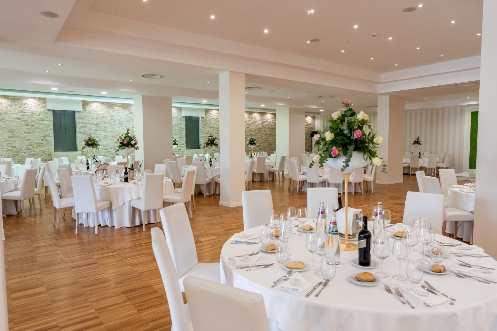 Ein Banketthaus mit runden Tischen, gedeckten Plätzen, weißen Stühlen und Blumenarrangements in der Mitte.