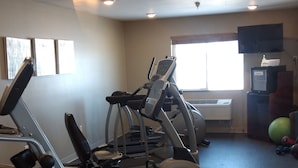 A gym with exercise equipment, a ceiling-mounted air vent, and a window with blinds.
