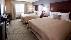 A hotel room with two beds, a desk, a television, and a window with curtains.