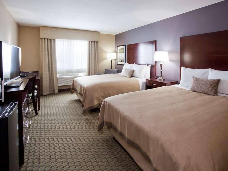 A hotel room with two beds, a desk, a television, and a window with curtains.