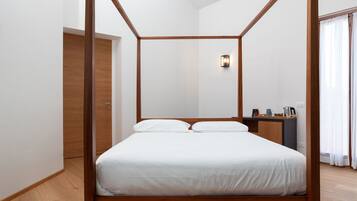A four-poster bed with white bedding in a modern room with wooden flooring and a small bedside table.