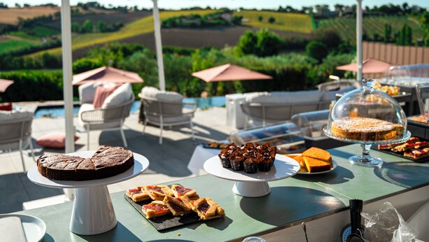 A dining table with various desserts and a pool view in the background. - A3Passi Agriturismo tra gli Ulivi (Ancona)