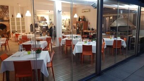 An indoor dining area with tables set for guests, a kitchen in the background, and a view through a glass wall. - A3Passi Agriturismo tra gli Ulivi (Ancona)