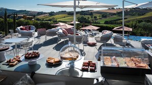 An outdoor dining area with tables, chairs, and umbrellas, overlooking a scenic landscape. - A3Passi Agriturismo tra gli Ulivi (Ancona)