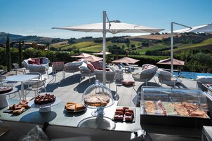 Un espacio de comedor al aire libre con mesas, sillas y sombrillas, con vistas a un paisaje pintoresco.