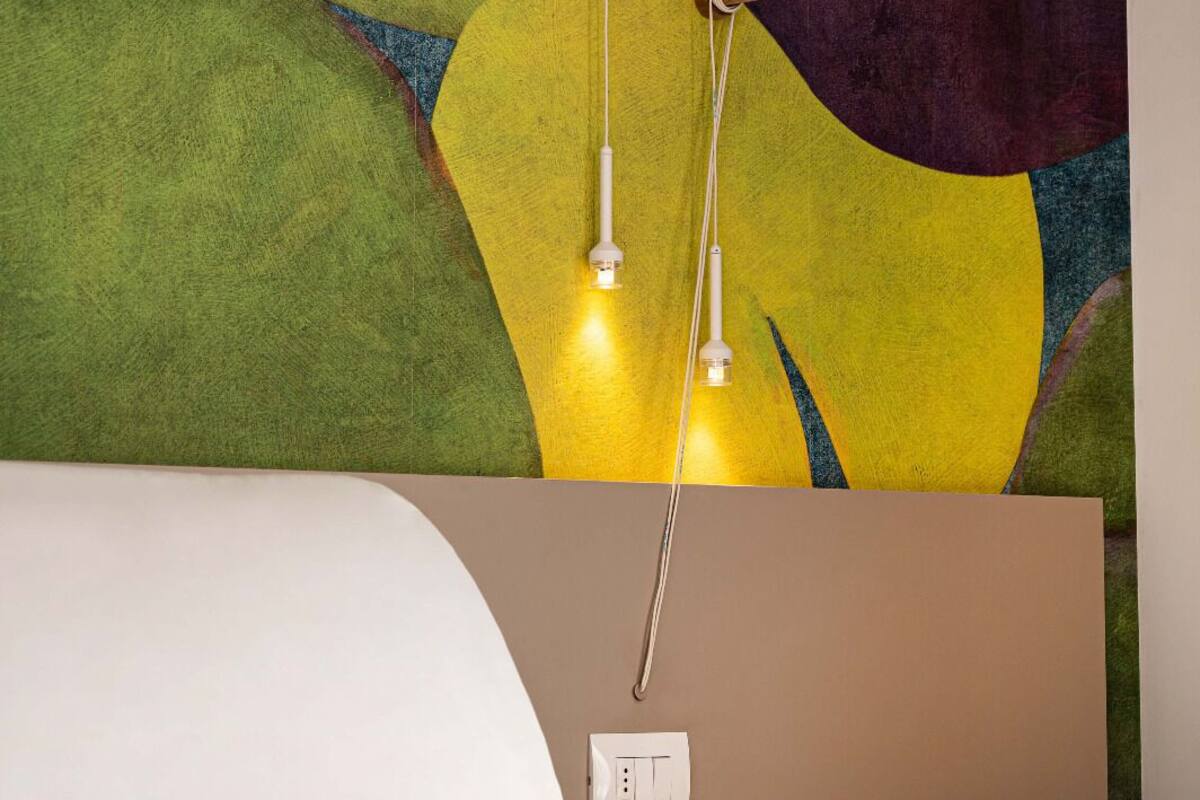 Una cama con cabecera blanca, una pared con arte abstracto e interruptor de luz.