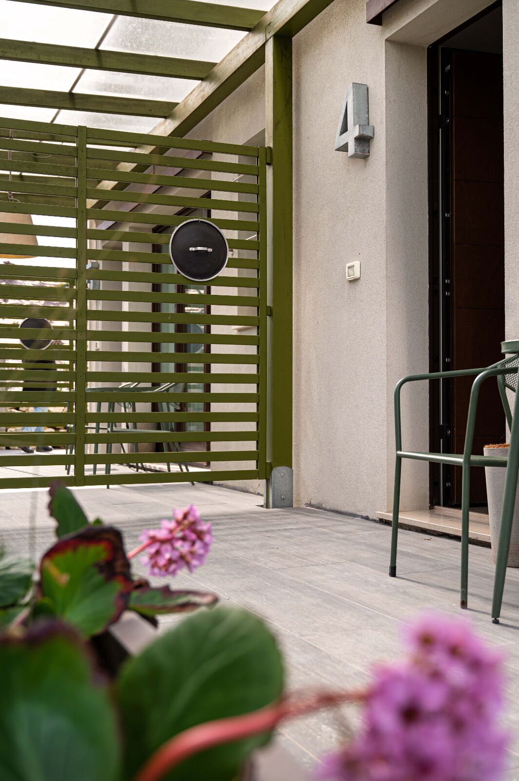 A covered outdoor area with a green metal gate, a door, and a chair.