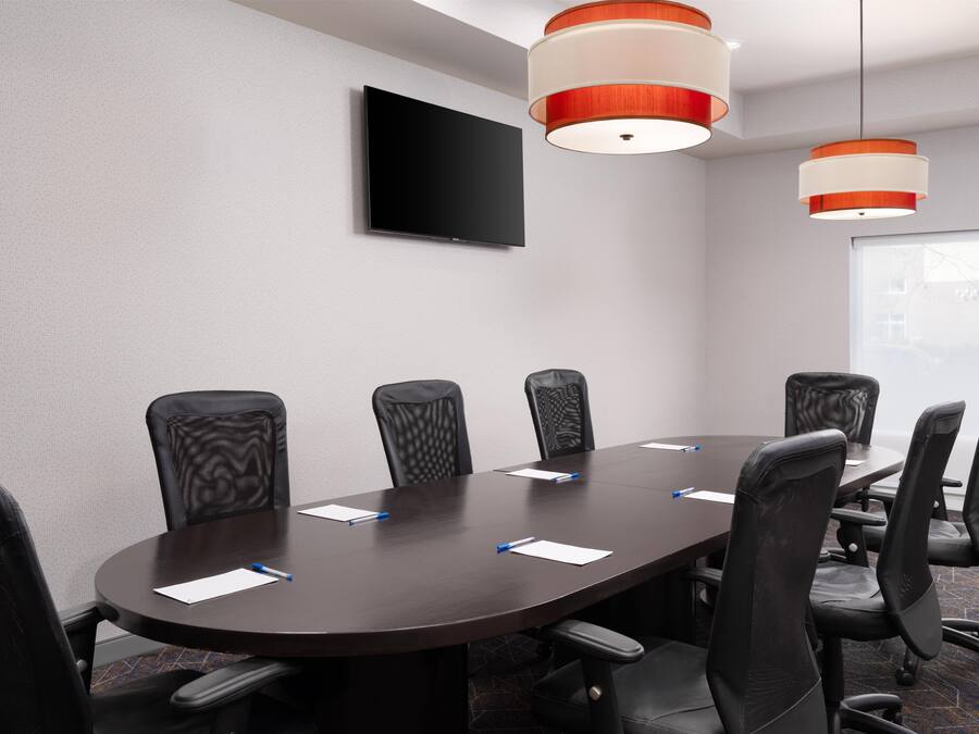 A conference room with a dark wooden table, black mesh chairs, and two pendant lights.