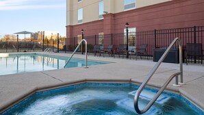 Una piscina con escaleras metálicas, sillas exteriores y un edificio con fachada roja al fondo.